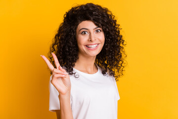 Wall Mural - Photo of young happy excited cheerful positive girl showing v-sign wear white t-shirt isolated on yellow color background