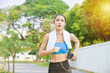 © gamelover - Beautiful asian woman in sportswear listening to music on earphones while running outdoors in the city.