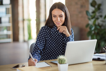 Photo of minded serious young brown haired woman write pen notebook work office laptop indoors in workplace