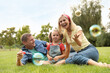 © New Africa - Happy family blowing soap bubbles in park on green grass