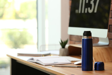 Poster - Modern thermos on wooden desk at workplace. Space for text