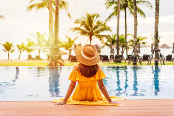 young woman traveler relaxing and enjoying the sunset by a tropical resort pool while traveling for 