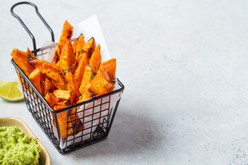 Wall Mural - Sweet potato fries in metal basket with guacamole, gray background. Vegan food concept.