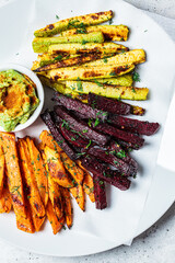 Canvas Print - Baked vegetable fries with zucchini, sweet potato and beetroot with guacamole on white plate, gray background. Vegan food concept.