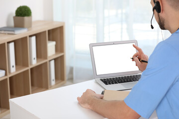 Canvas Print - Doctor with headset consulting patient online at desk in clinic, space for text. Health service hotline