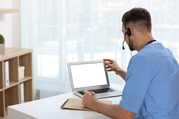 Canvas Print - Doctor with headset consulting patient online at desk in clinic, space for text. Health service hotline