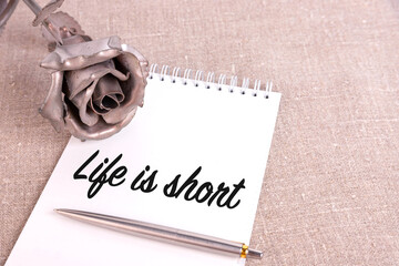 Wall Mural - Life is short, the text is written in a notebook lying on a linen linen and an iron rose flower.