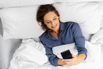 Poster - technology, internet, communication and people concept - happy young woman texting on smartphone lying in bed at home in morning