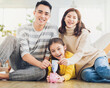 © Tom Wang - Father, mother and daughter holding a piggy bank and money  at home. Family and saving for future concept.