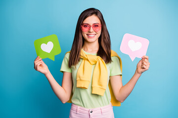 Poster - Photo of young lovely pretty attractive happy smiling girl in funky glasses hold heart icons isolated on blue color background