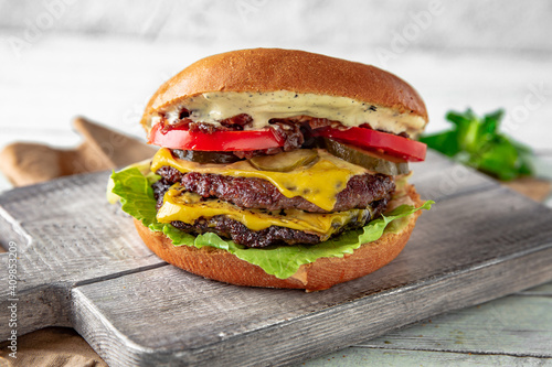 Delicious, juicy hamburger, cheeseburger with beef, cheese, baked vegetables and fruits, onion jam, sauces on wooden background, rustic style.
