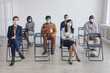 © Seventyfour - Full length multi-ethnic group of business people wearing masks and social distancing while sitting on chairs in audience at business conference or seminar