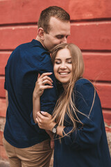 Wall Mural - Happy young family on the background of a red wall. Young woman laid her head on her man's shoulder