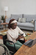 © Seventyfour - Vertical high angle portrait of young African-American woman using wheelchair while working from home with childrens toys in background