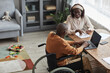 © Seventyfour - High angle portrait of African-American man using wheelchair working from home with wife, copy space