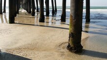 Wooden Piles Under Boardwalk, Old Pier In Oceanside, California Coast USA. Pilings, Pylons Or Pillars Below Retro Vintage Bridge, Waterfront Promenade. Ocean Waves, Sea Water Tide And Sand Beach.