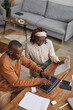 © Seventyfour - Vertical high angle portrait of young African-American couple working from home together and using laptop, copy space