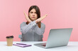 © khosrork - Upset bossy woman office worker sitting at workplace crossing hands showing x sign, rejecting and finishing sexual harassment at work. Indoor studio shot isolated on pink background