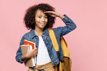 Smiling little african kid school girl 12-13 years old in casual clothes backpack hold book hold hand at forehead look far away distance isolated on pastel pink background Childhood education concept.