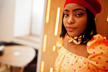 Wall Mural - Elegant afro american woman in red french beret, big gold neck chain polka dot blouse pose indoor.