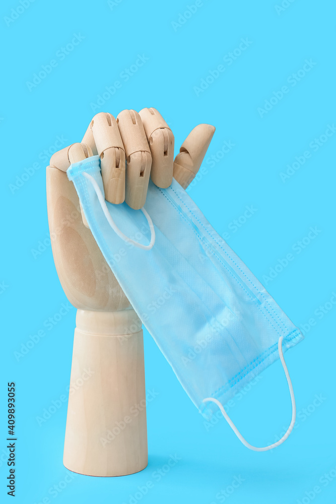 Wooden hand with medical mask on color background