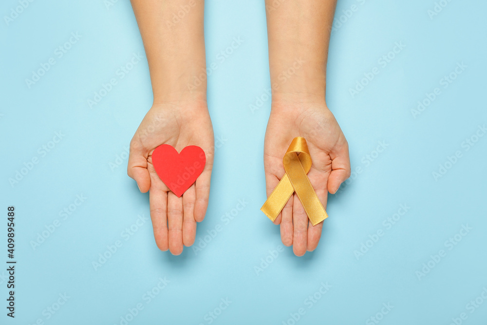 Hands with red heart and golden ribbon on color background. Childhood cancer awareness concept