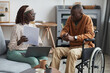 © Seventyfour - Portrait of African-American couple with handicapped man using wheelchair working from home together in modern interior