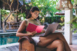 © BullRun - Stylish ethnic woman working on laptop sitting at poolside of tropical hotel
