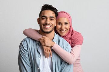Portrait Of Muslim Couple Embracing Over Grey Background And Smiling At Camera