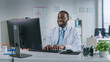 © Gorodenkoff - Happy Smiling African American Medical Doctor is Working on a Computer in a Health Clinic. Physician in White Lab Coat is Browsing Medical History Behind a Desk in Hospital Office.