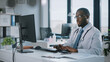 © Gorodenkoff - Calm African American Family Medical Doctor in Glasses is Working on a Desktop Computer in a Health Clinic. Physician in White Lab Coat is Browsing Medical History Behind a Desk in Hospital Office.