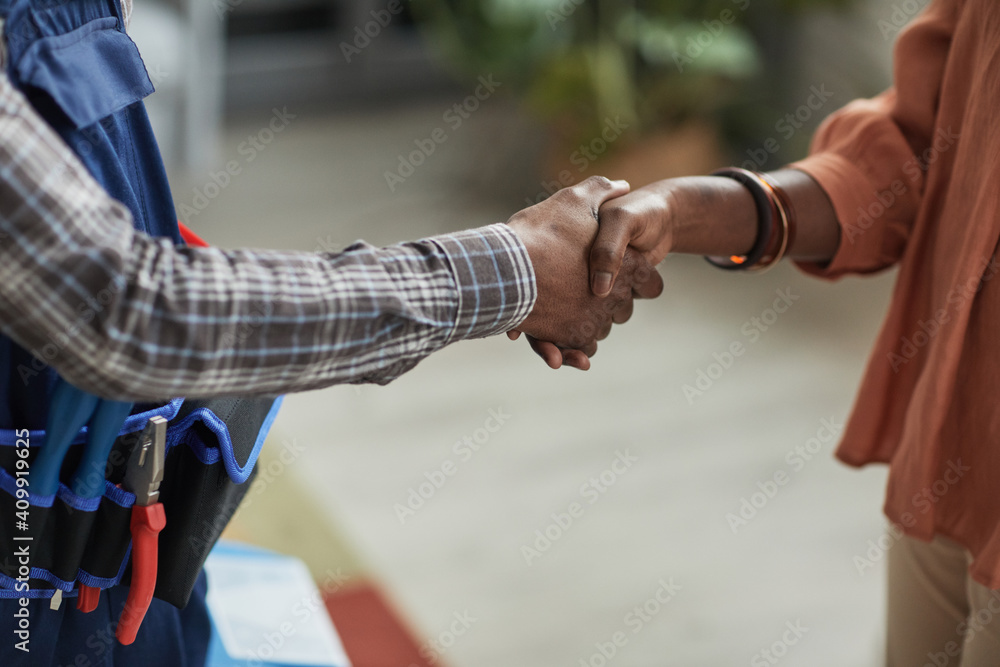 Close up of unrecognizable African-American woman shaking hands with handyman standing in home interior, copy space - obrazy, fototapety, plakaty 