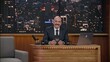© supamotion - Late-night talk show host sitting behind his table and performing his monologue, looking into camera. TV broadcast style show