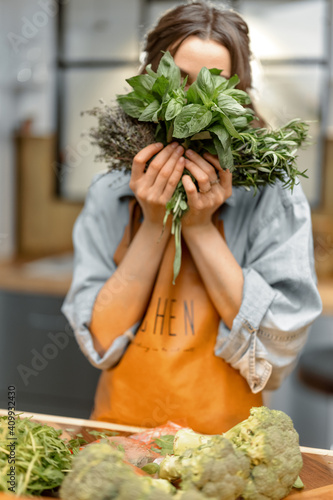 Portrait of cheerful woman in apron holding fresh spicy herbs basil, rosemary, thyme and cover her face. On the kitchen. Healthy cooking concept. High quality photo © rh2010