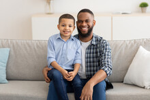 Little Black Boy Sitting On Dad's Knees Posing At Home