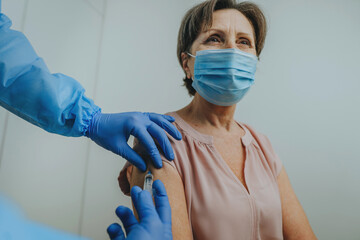 Doctor in protective overall and gloves making COVID-19 vaccination