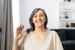 © Face Stock - Webcam view of a smiling senior woman waving hello into the camera, older female teacher look at camera conducts online lesson, webinar. Video meeting with a grey-haired grandmother