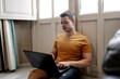 © Alberto Ortega/ADDICTIVE STOCK - Focused male freelancer in casual outfit sitting on floor near window and typing on laptop while working remotely from home