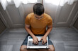 © Alberto Ortega/ADDICTIVE STOCK - From above focused male freelancer in casual outfit sitting on floor near window and typing on laptop while working remotely from home