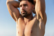 © Andres Victorero/ADDICTIVE STOCK - Shirtless bearded male athlete with strong body standing with raised arms on background of blue sky and looking away