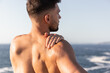 © Andres Victorero/ADDICTIVE STOCK - Back view of male bodybuilder with muscular naked torso warming up and stretching arms before workout near sea in summer