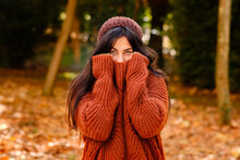 Young Female In Knitted Hat Covering Face With Warm Sweater While Standing In Forest In Cold Autumn Day