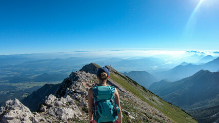 a woman with big backpack hiking along a steep pathway to the metal cross with a panoramic view on t