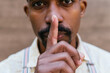 © David Munoz/ADDICTIVE STOCK - Crop African American male covering mouth with finger and showing silence sign while looking at camera