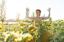 Smiling Female In Dress Practicing Yoga In Goddess Pose While Standing With Mudra Hands In Blooming Sunflower Field In Summer