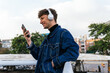 © David Munoz/ADDICTIVE STOCK - Side view of positive young male listening to music in wireless headphones browsing on smartphone while enjoying weekend in street