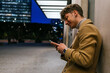 © David Munoz/ADDICTIVE STOCK - Side view of smiling handsome male leaning on building and messaging on social media via smartphone in evening in city