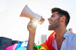 © David Munoz/ADDICTIVE STOCK - Side view of eccentric gay male with rainbow LGBT flag standing in city and yelling in loudspeaker with closed eyes