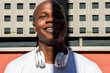 © David Munoz/ADDICTIVE STOCK - Positive African American male with headphones standing near urban building and looking away while enjoying summer weekend