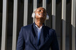© David Munoz/ADDICTIVE STOCK - Dreamy African American male entrepreneur in suit standing in city with closed eyes and enjoying songs in wireless headphones